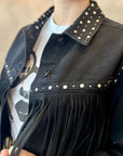 Person wearing a black studded jacket with fringe details.