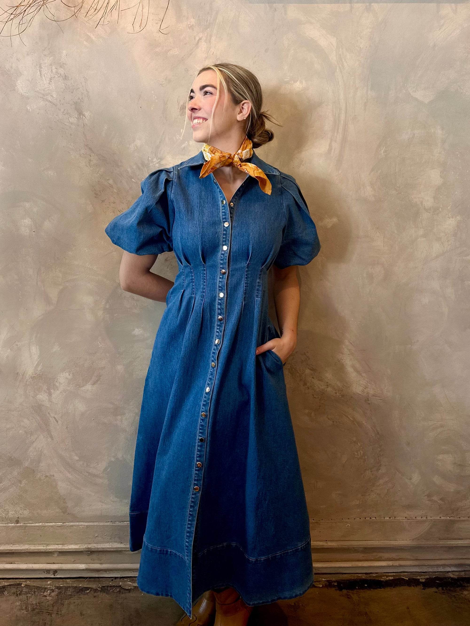 Woman wearing a blue dress against a textured wall.