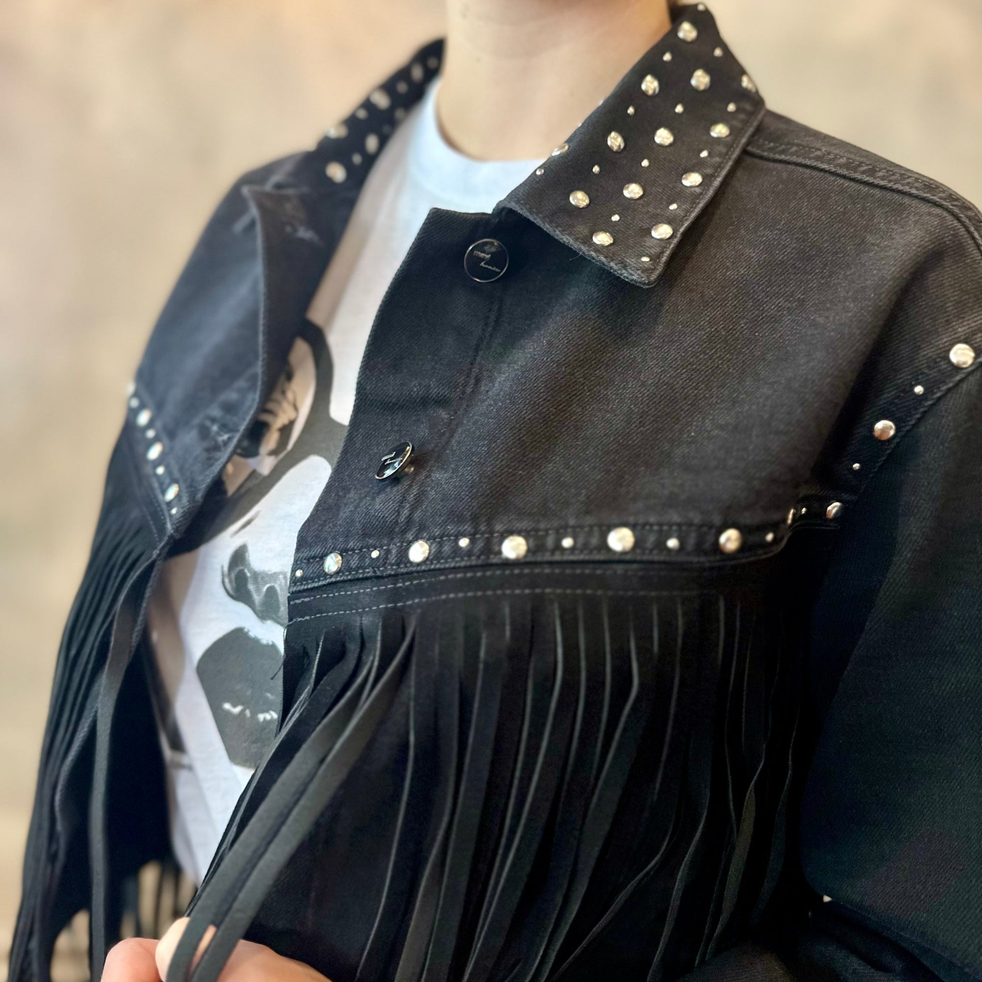 Person wearing a black studded jacket with fringe details.