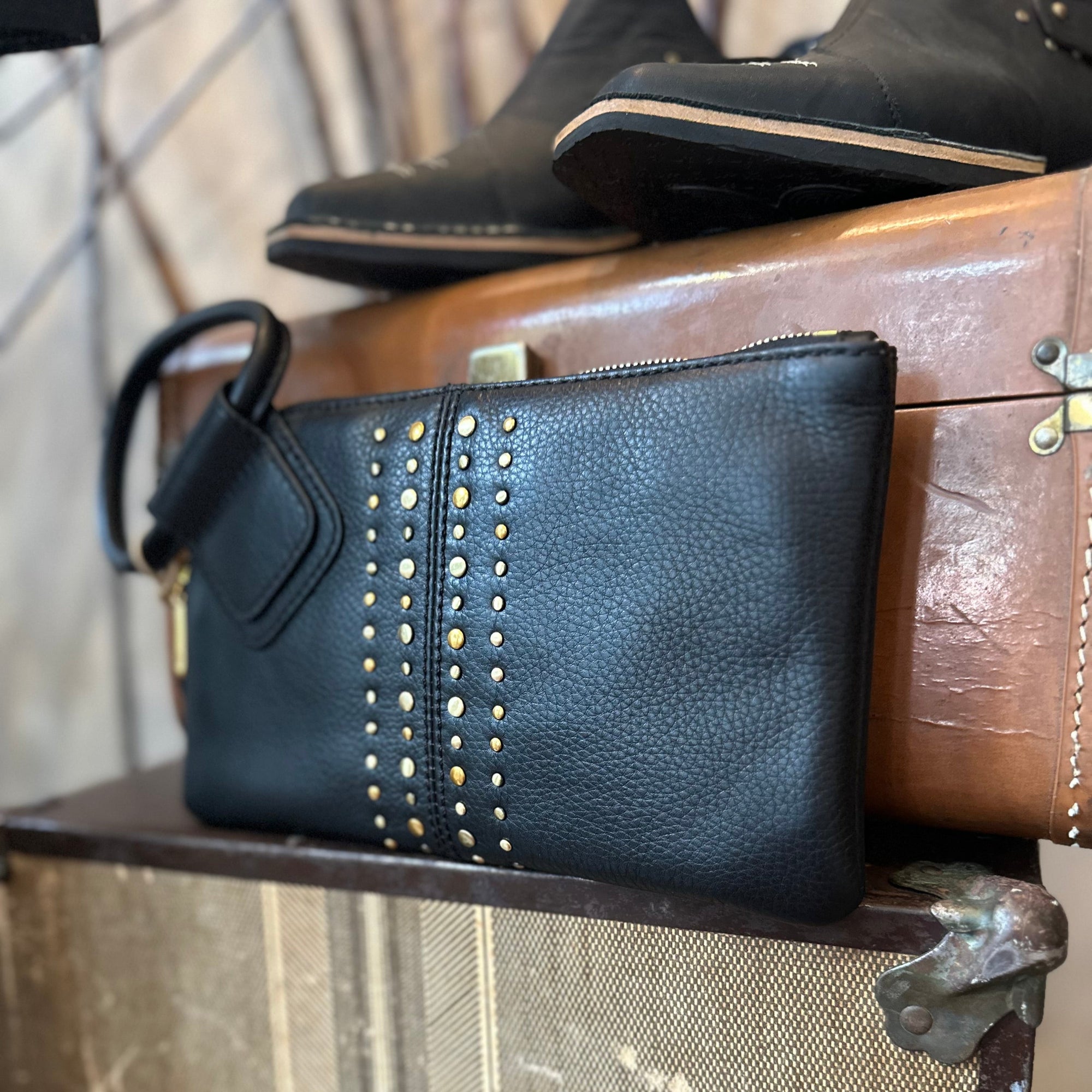 Black leather clutch with gold studs on a vintage suitcase
