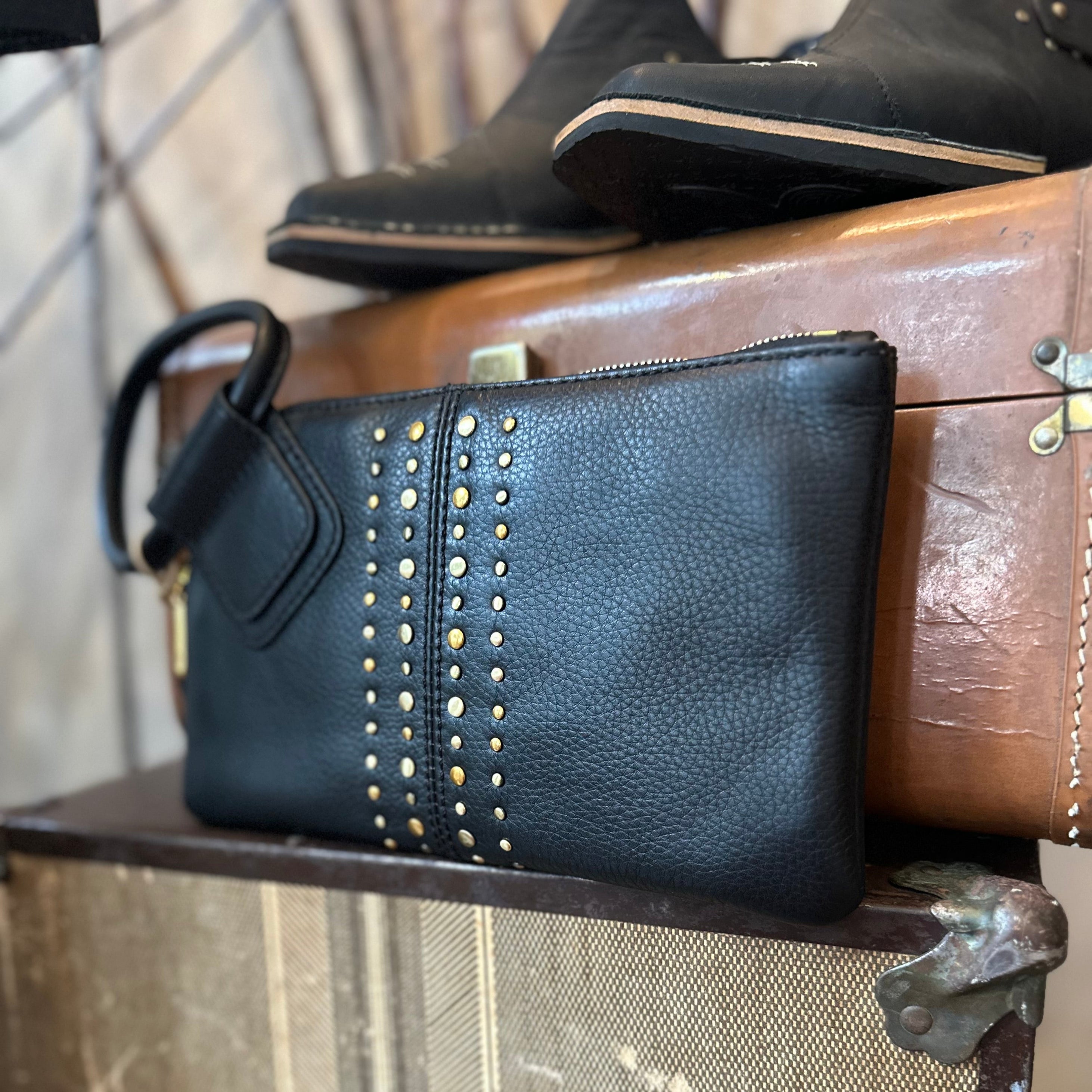 Black leather clutch with gold studs on a vintage suitcase