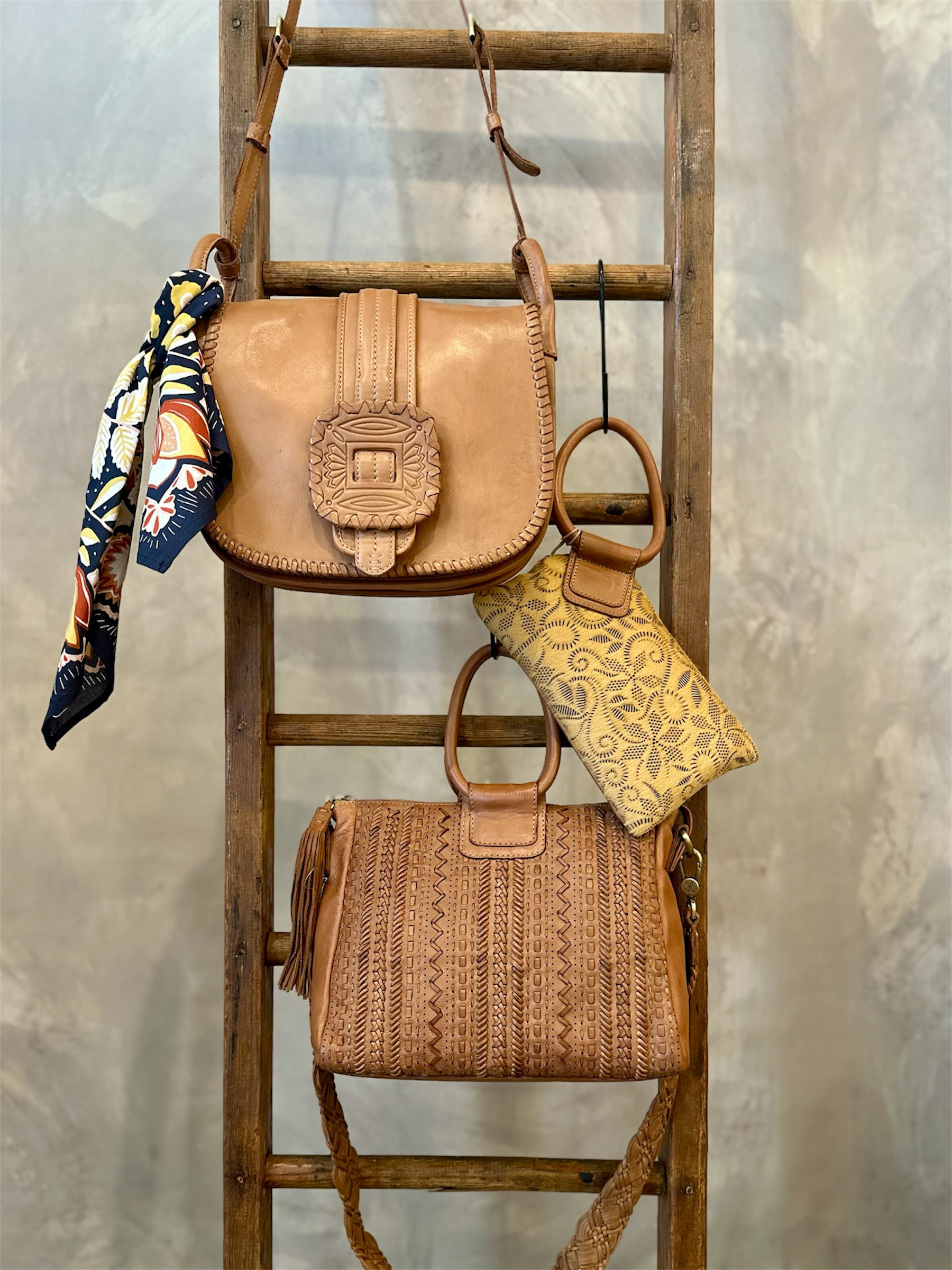 Three handbags on a wooden ladder against a textured wall.